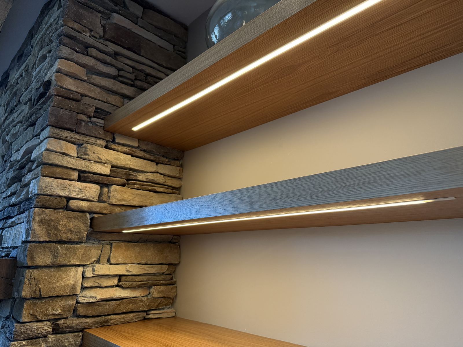 Lit floating shelves built into a stone fireplace wall